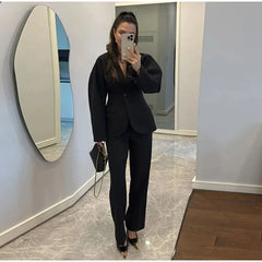 Woman taking a mirror selfie wearing a black suit in a room with a marble floor and white walls.