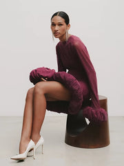 Woman in a burgundy dress with ruffled sleeves sitting on a wooden stool against a white background