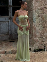 Woman in a light green strapless dress standing against a stone wall.