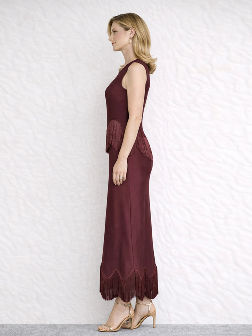 Side view of a burgundy sleeveless O-neck maxi dress with fringe trim.