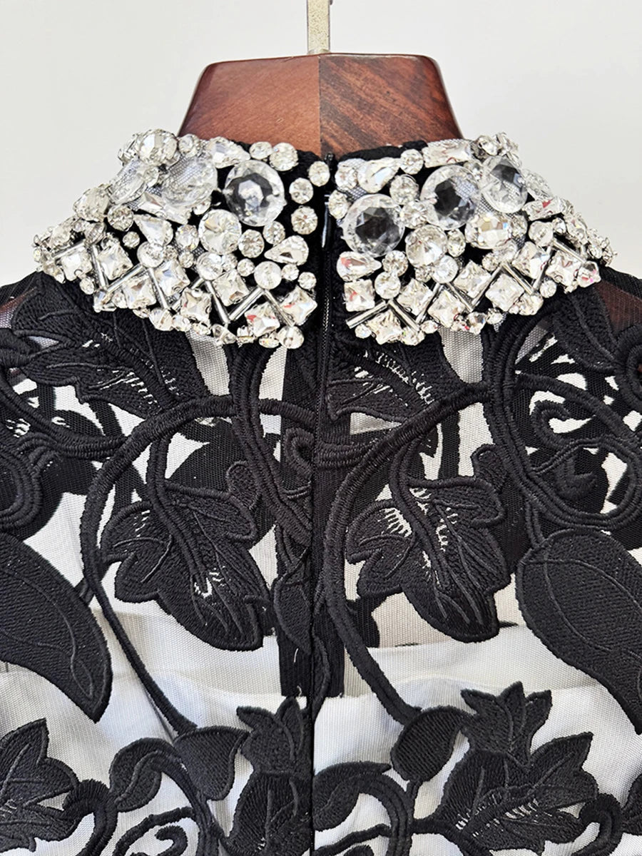 Black lace garment with silver embellishments on a mannequin against a white background