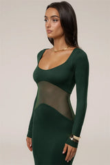 Woman wearing a green dress with sheer panels on a plain background