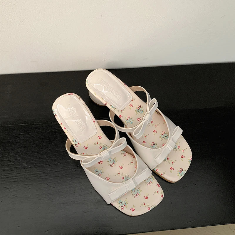 Pair of white floral sandals on a black surface with a white background