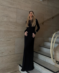Woman in a black dress standing on a staircase with a beige wall background