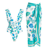 White one-piece swimsuit with abstract blue and green dots and a matching wrap skirt.