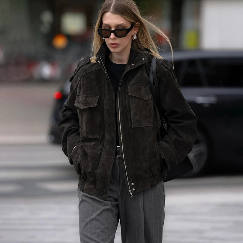 Woman wearing a dark jacket and sunglasses on a city street.