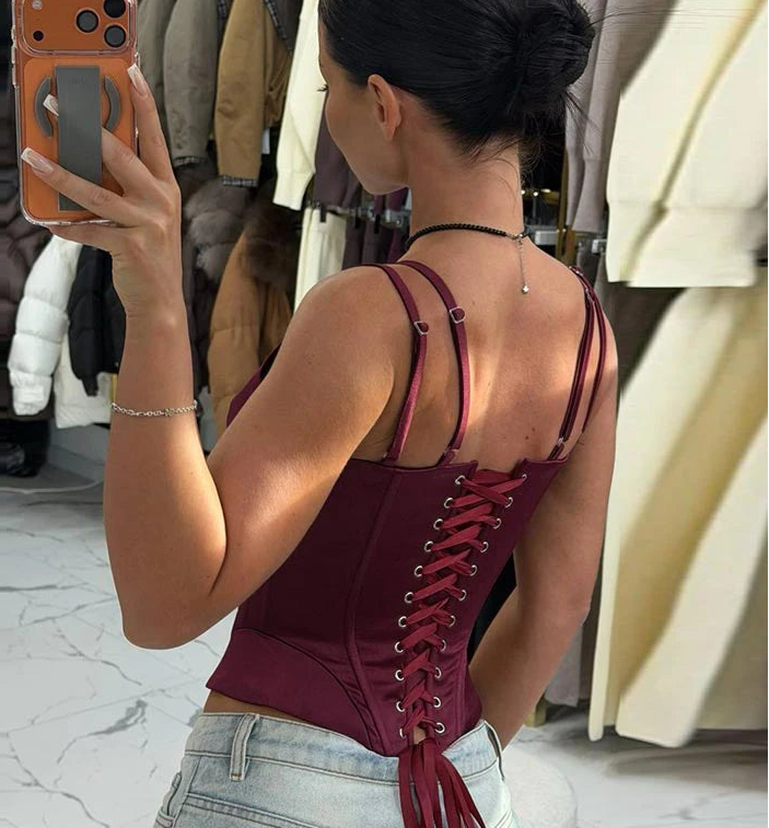 Woman taking a mirror selfie wearing a maroon lace-up top in a clothing store.