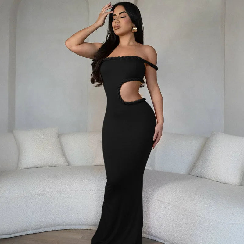 Woman in a black off-shoulder dress with cut-out design standing in a room with white walls and furniture.