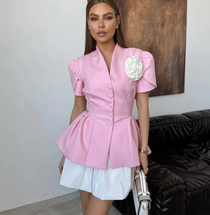 Woman wearing a pink blazer with a decorative brooch in an indoor setting.