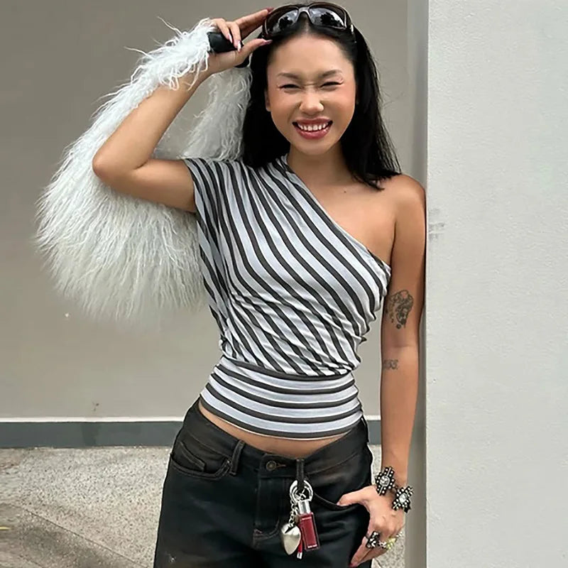 Woman wearing a black and white striped top with a white feathered item, standing against a plain background.