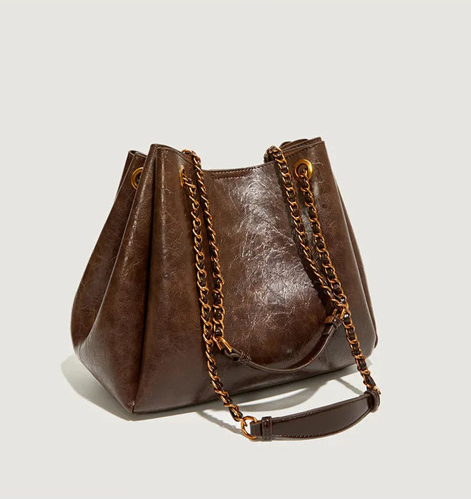 Brown leather handbag with chain detail on a light gray background