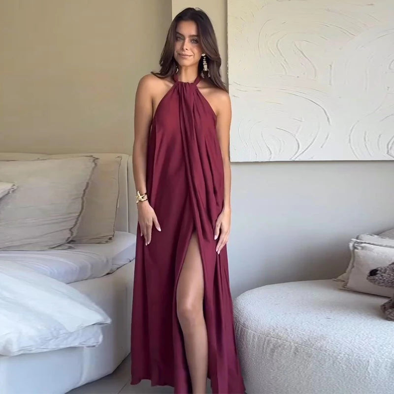 Woman wearing a burgundy halter neck dress with a slit, standing in a room with a white couch and decorative pillows.