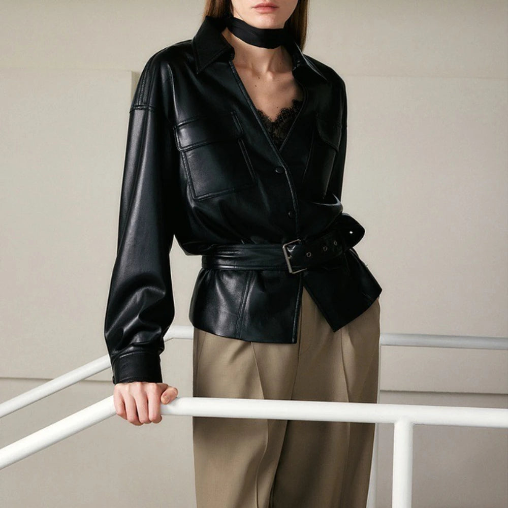Person wearing a black leather jacket and beige pants against a neutral background
