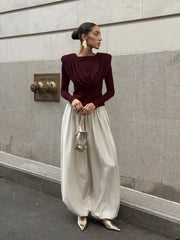 Woman in burgundy top and white pants standing against a gray wall.