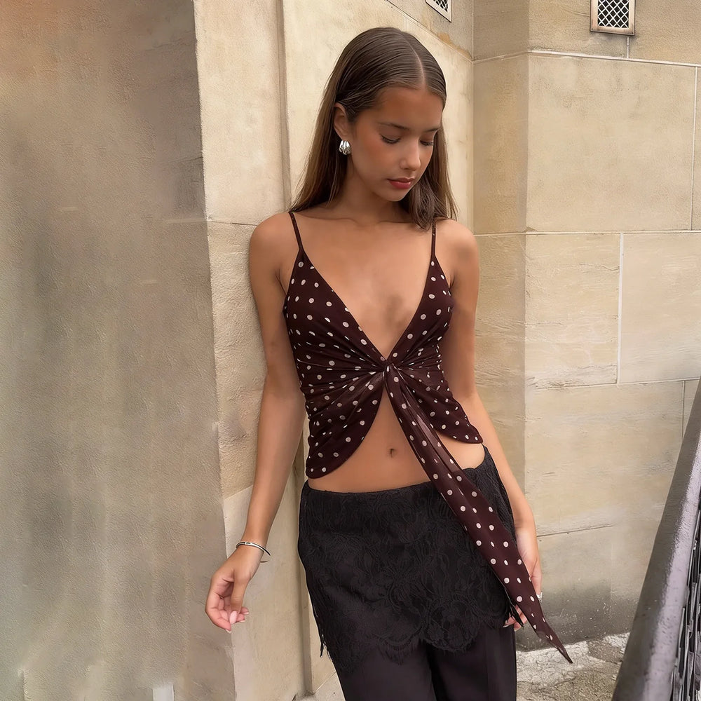 Woman wearing a polka dot top and black pants against a stone wall.