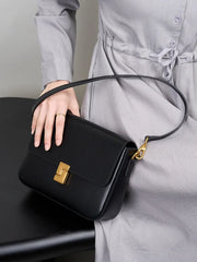 Person holding a black handbag with a gold clasp against a neutral background