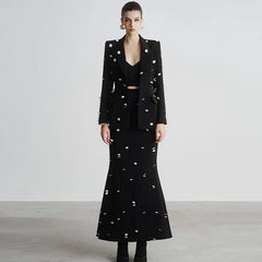 Woman wearing a black outfit with white embellishments against a plain background