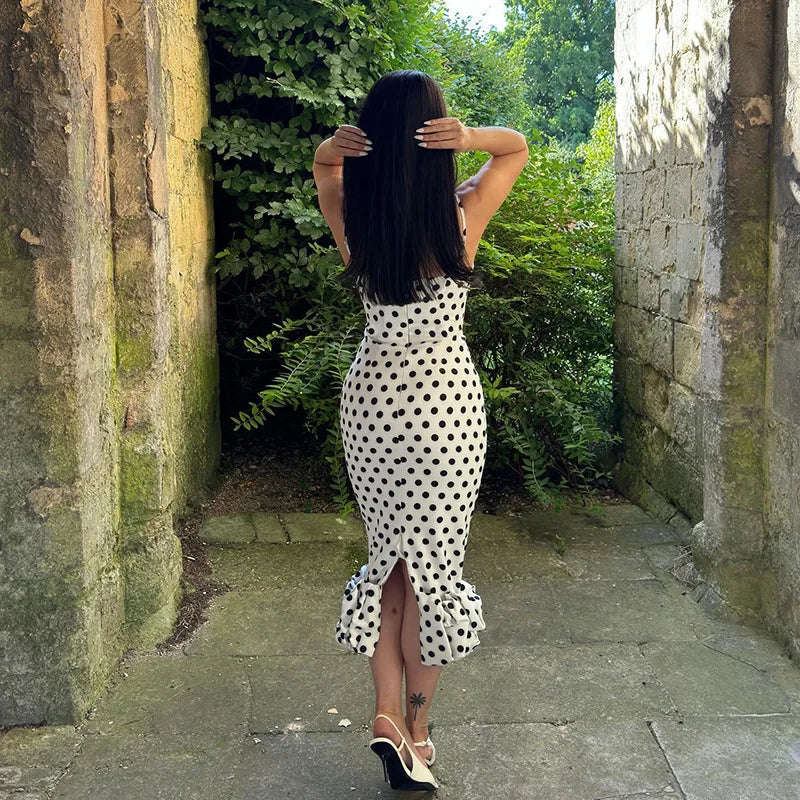 Woman in a polka dot dress walking through a stone archway with greenery.
