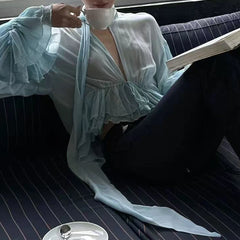 Close-up of a woman wearing a sheer ruffled halter blouse, holding a teacup.