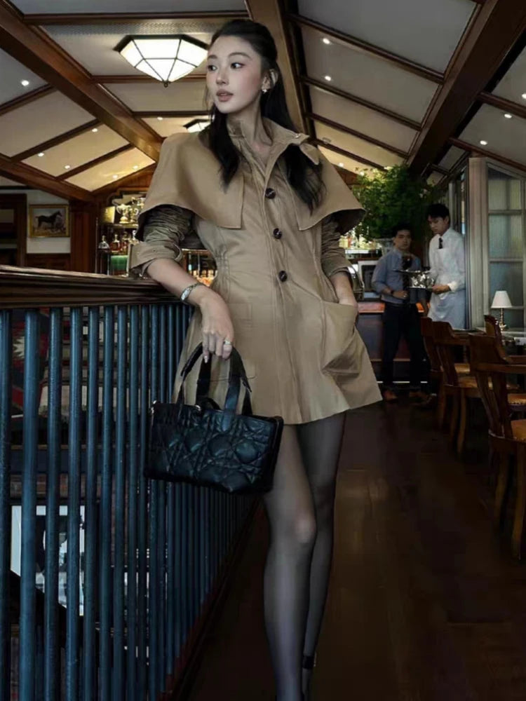 Woman in a beige trench coat holding a black handbag in an indoor setting