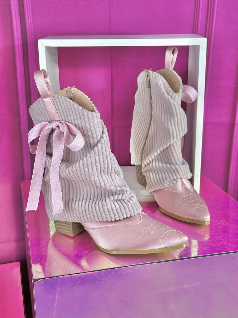 Pink ribbed knit slouchy boots with satin pointed toe and bow accent on display.