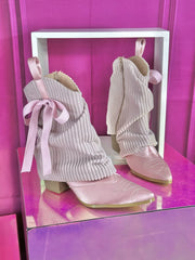 Pink ribbed knit slouchy boots with satin pointed toe and bow accent on display.