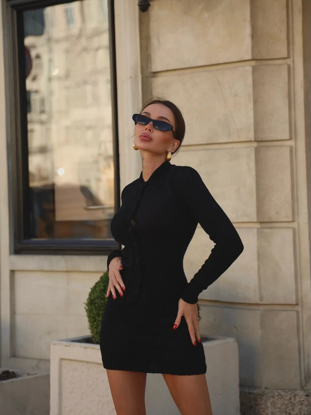 Woman in a black dress and sunglasses standing in front of a building.