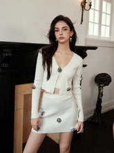 Woman wearing a white outfit with black buttons in an elegant room.