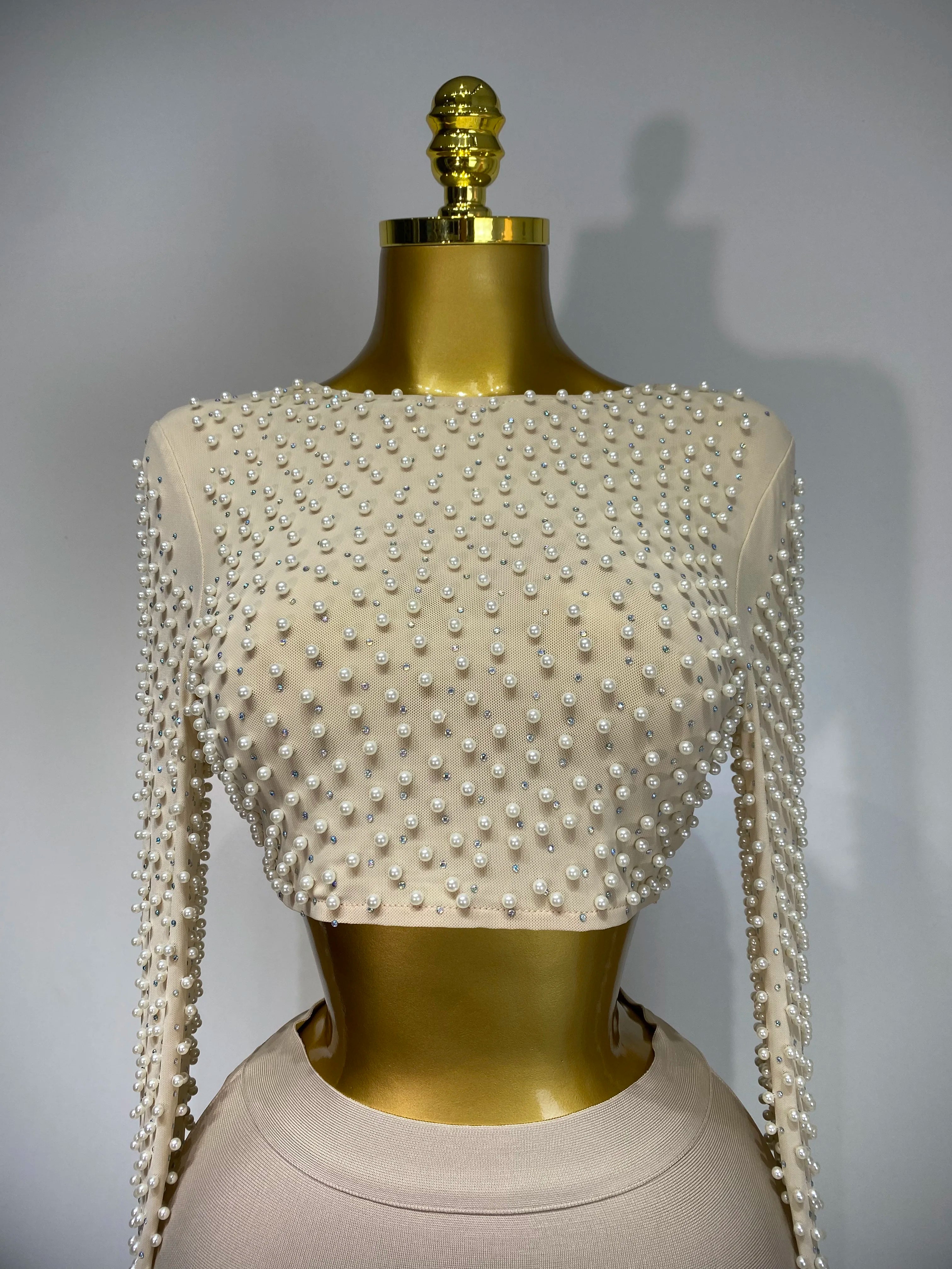 Mannequin wearing a white beaded top with long sleeves on a gray background
