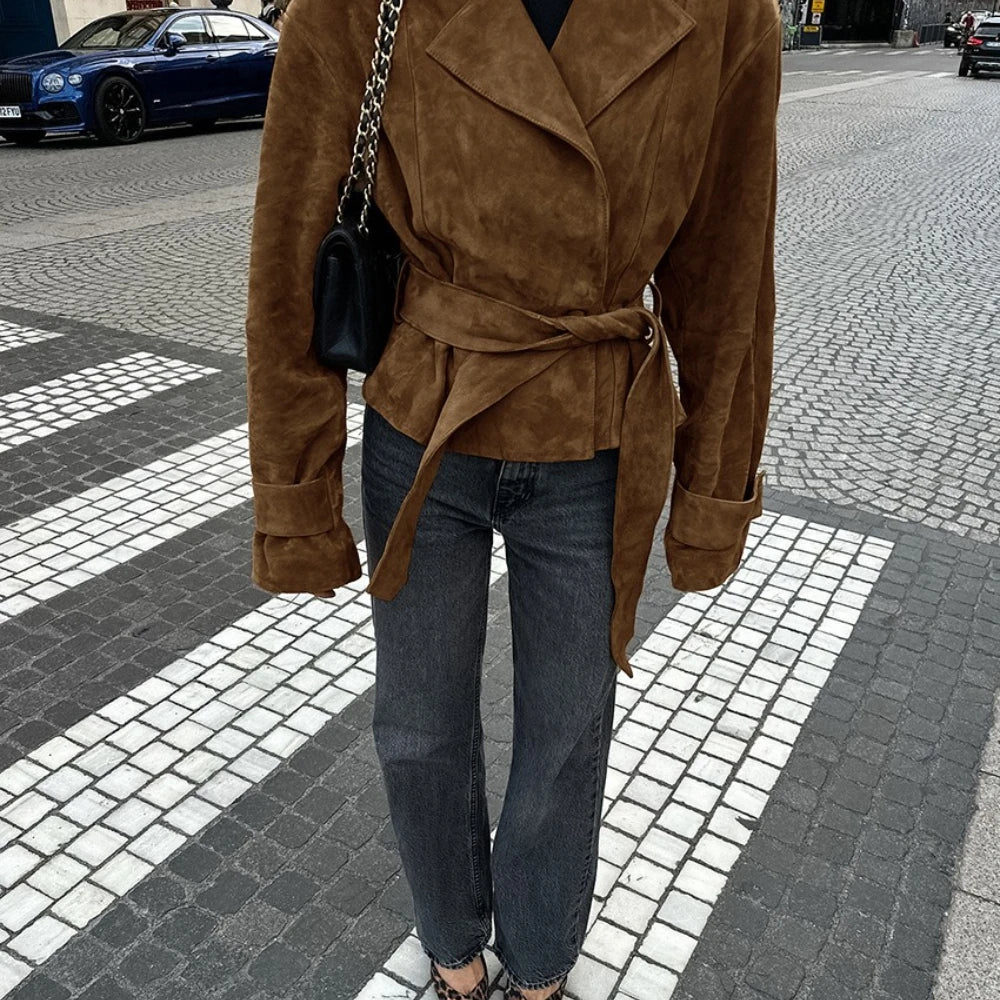 Person wearing a brown suede coat and blue jeans on a city street.