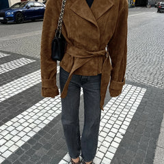 Person wearing a brown suede coat and blue jeans on a city street.