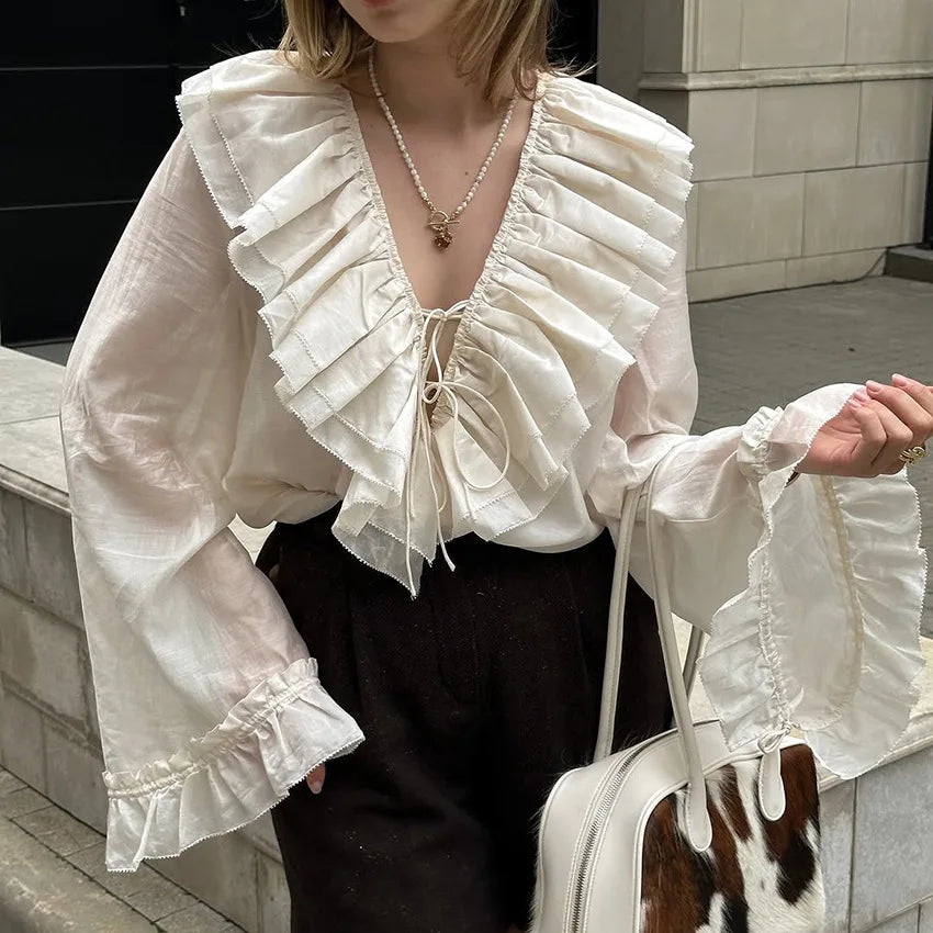 Person wearing a white ruffled blouse with long sleeves, standing outdoors.