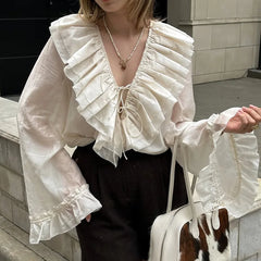 Person wearing a white ruffled blouse with long sleeves, standing outdoors.