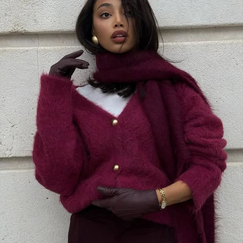 Woman wearing a burgundy cardigan with gold buttons against a light-colored wall.