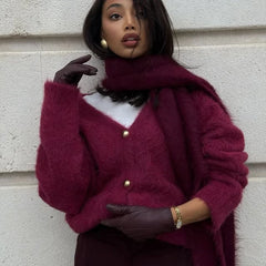 Woman wearing a burgundy cardigan with gold buttons against a light-colored wall.