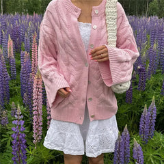 Person wearing a pink cardigan and white dress standing in a field of purple flowers