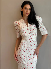 Woman wearing a white dress with red patterns against a plain background