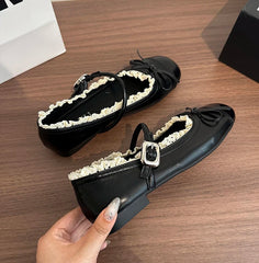 Silver ballet flats with a round toe, lace trim, and butterfly knot detail, paired with white socks.