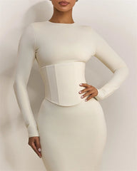 Woman wearing a fitted white dress with a waistband against a plain background