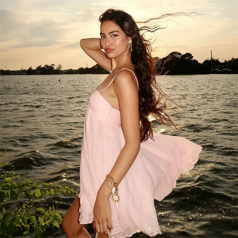 Woman in a pink dress standing by a body of water with a sunset in the background