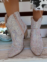 Beige cowboy boots with rhinestone embellishments on a wooden floor.