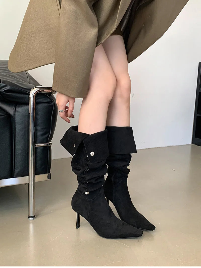 Person wearing black knee-high boots with a plain background