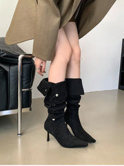 Person wearing black knee-high boots with a plain background