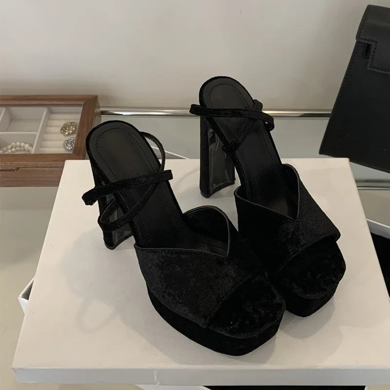Black suede platform sandals on a white surface with a neutral background