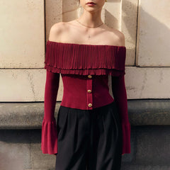 Person wearing a burgundy off-shoulder top with ruffled details against a stone wall.