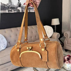 Brown handbag held in front of a living room setting with a couch and lamp.