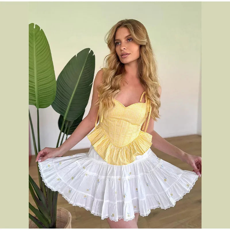 Woman wearing a yellow top and white skirt with ruffled layers, standing indoors.