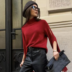 Woman wearing a red sweater and black pants, holding a black clutch against a building background.