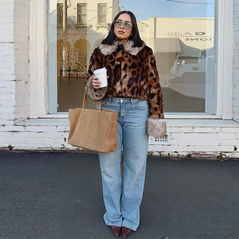 Woman wearing a leopard print jacket and blue jeans, holding a beige tote bag, standing in front of a building.