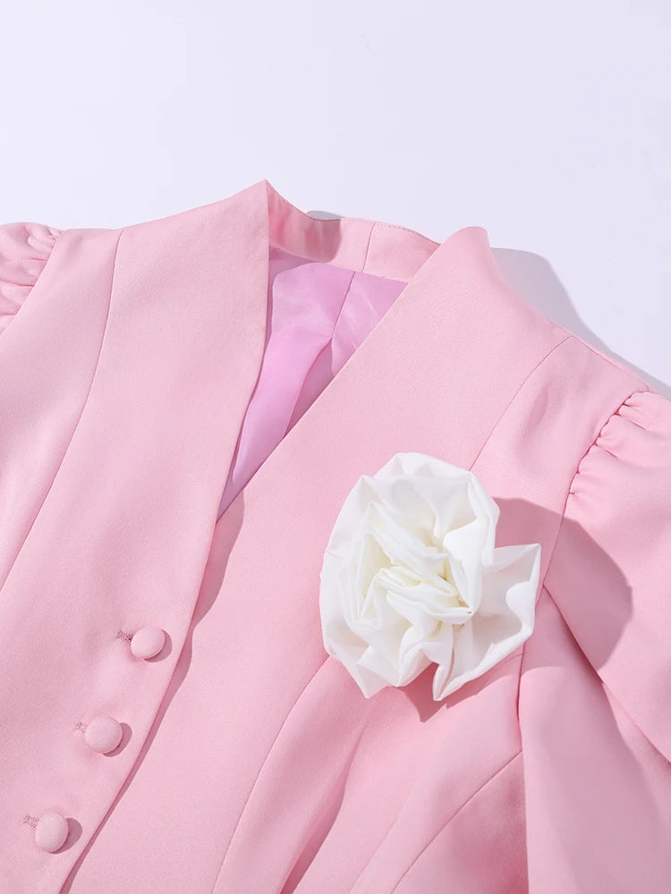 Pink blazer with a white floral accessory on a light gray background